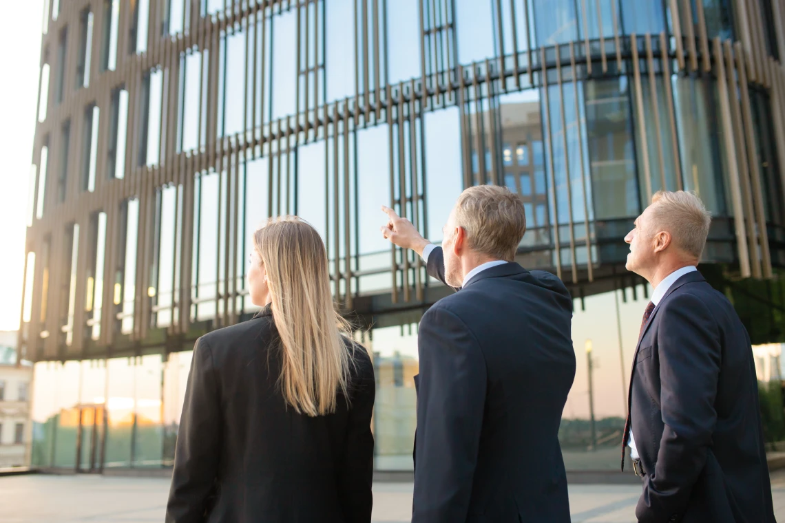 grupo de socios comerciales en trajes formales apuntando al edificio de oficinas reuniendose al aire libre discutiendo bienes raices vista trasera concepto de bienes raices comerciales